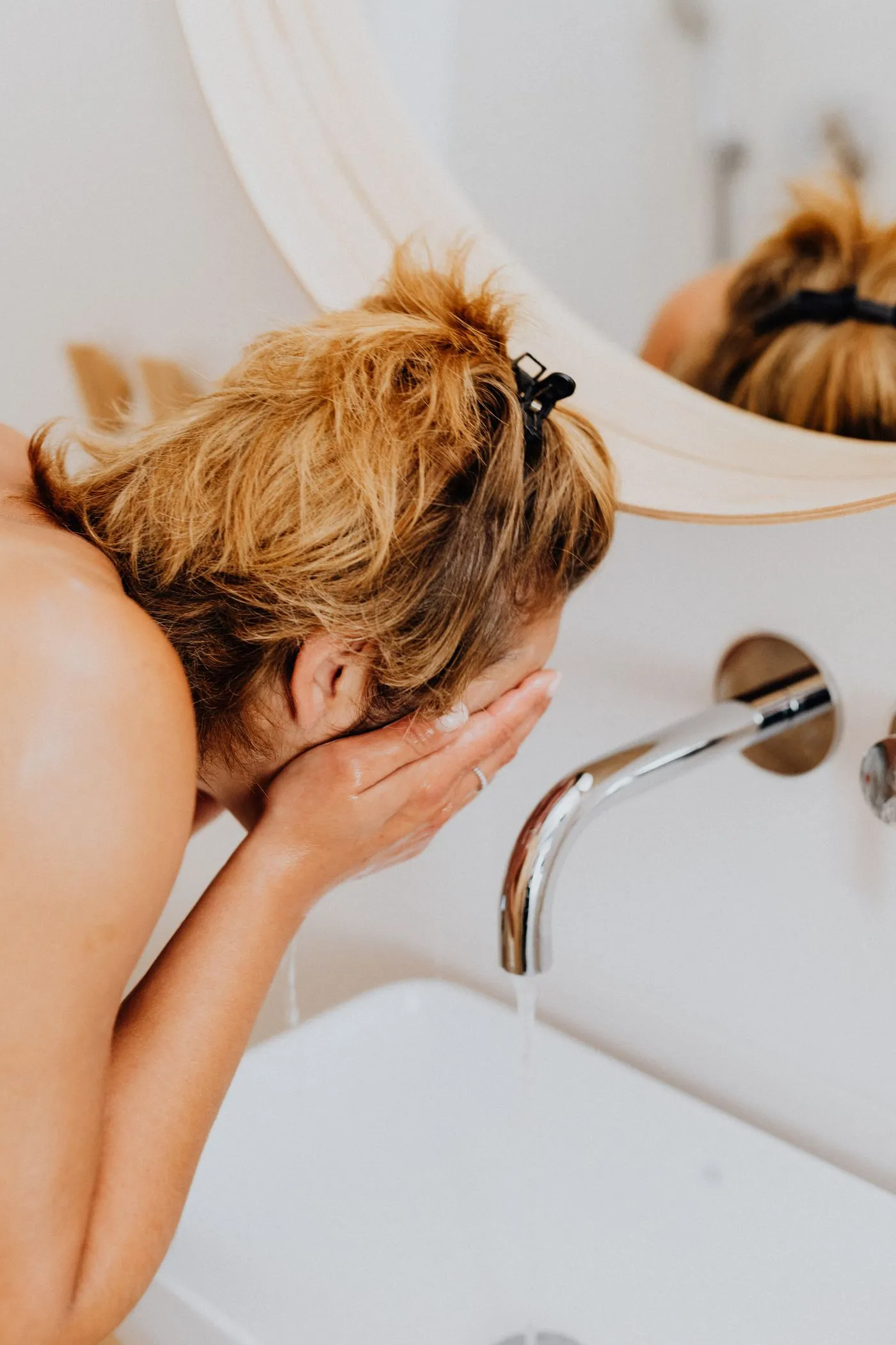 Mujer lavándose el rostro con agua en el baño